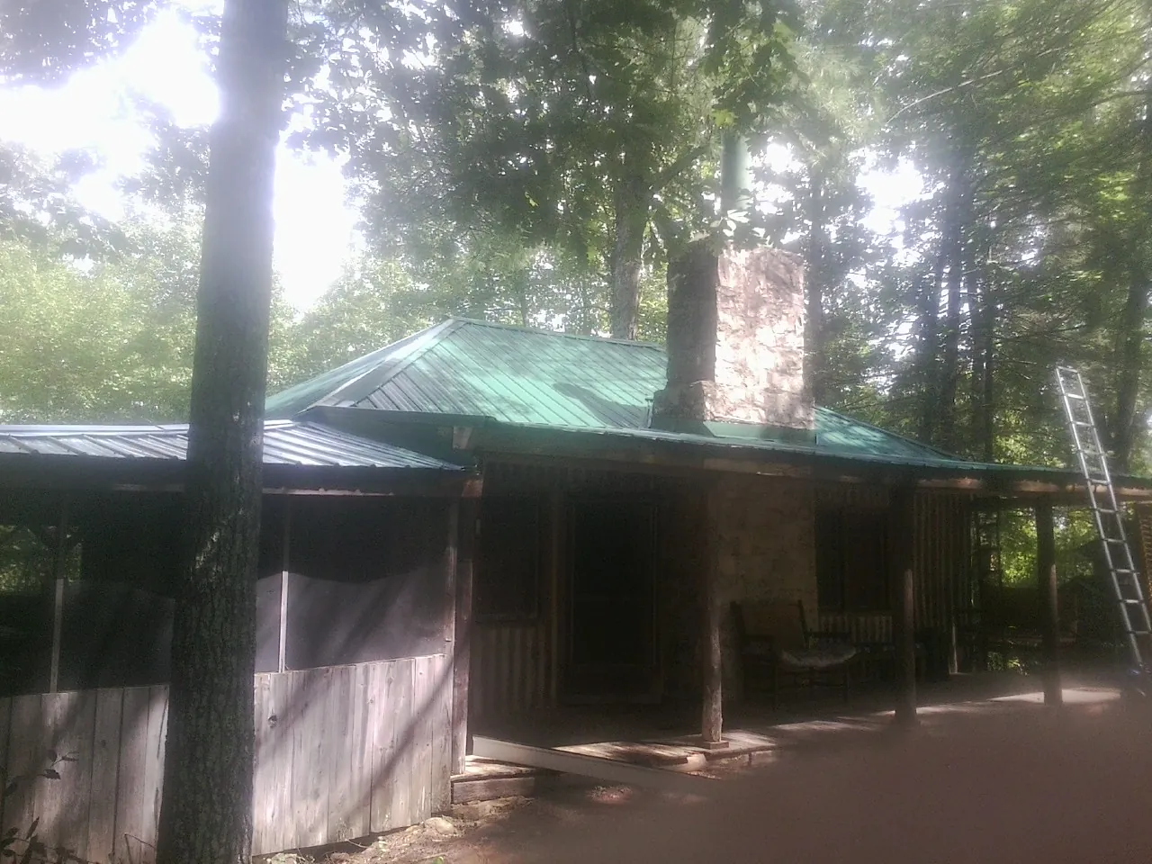Green metal roof and stone chimney above a log cabin porch in Weston